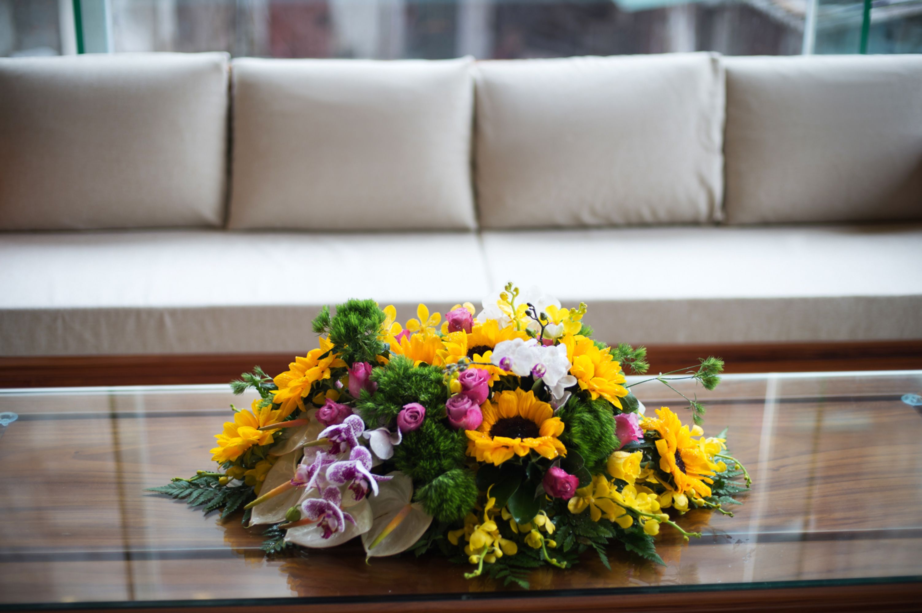 A floral arrangement on a glass table in front of a beige sofa.
