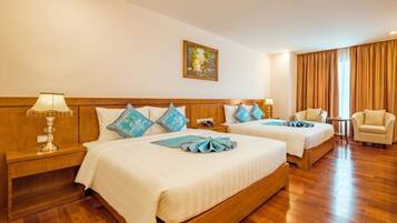 A hotel room with two beds, wooden headboards, a painting on the wall, a desk with a lamp, and a chair.