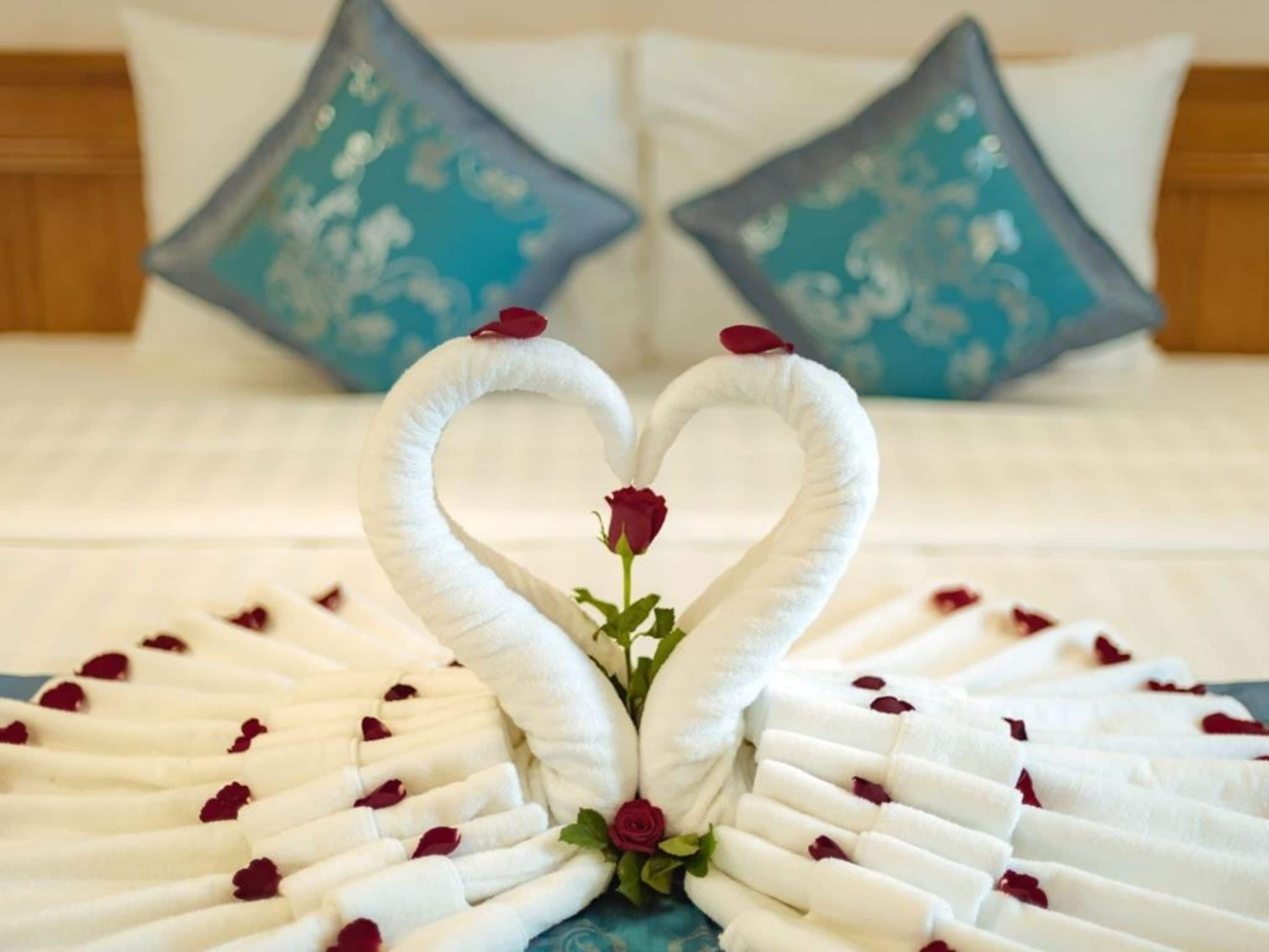 A bed with white linens and a heart-shaped towel arrangement with roses.