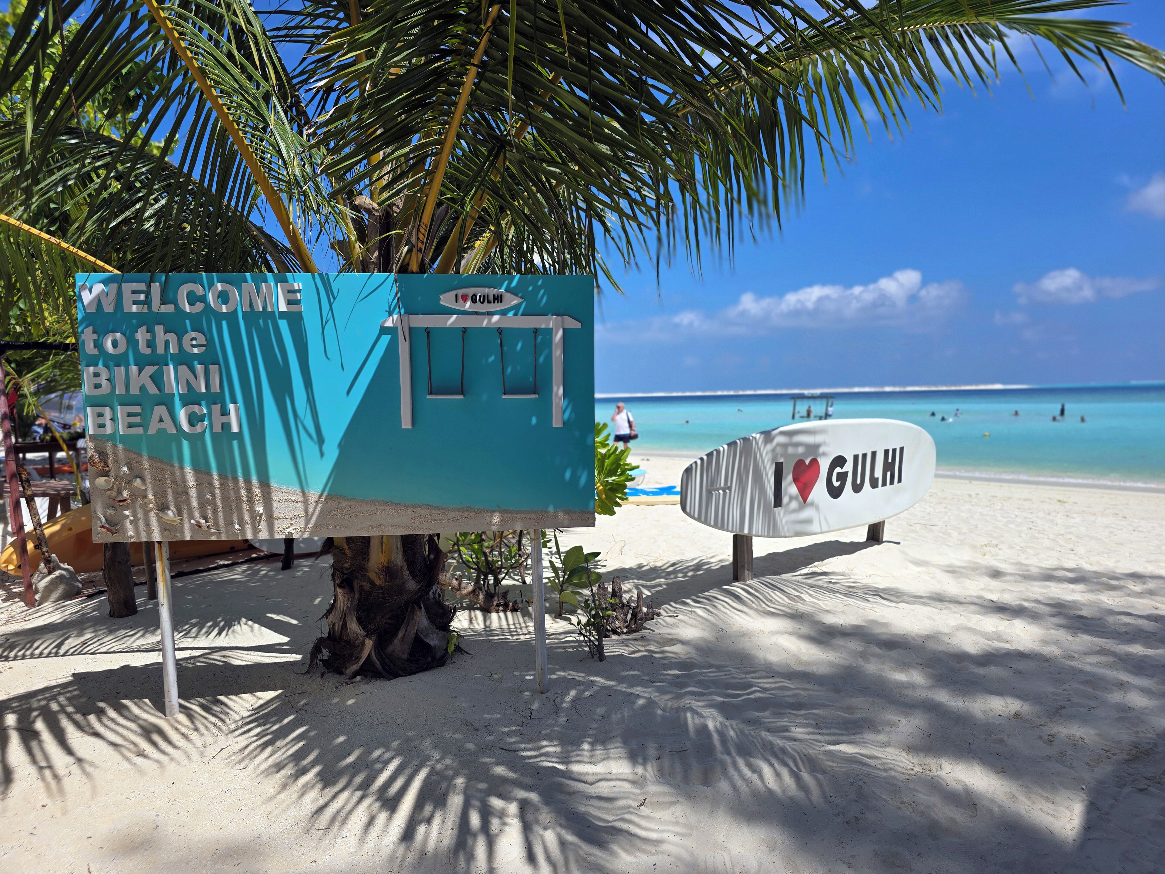 Een strandbord met 'WELCOME to the BIKINI BEACH' en 'I ♥ GULHI' erop.