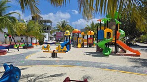 A playground with various play structures, including swings and slides, surrounded by palm trees and buildings. - Tropic Tree Hotel Maldives (Gulhi)
