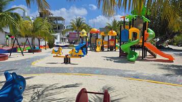 Kids can play on swings, slides, and climbing elements in this outdoor playground surrounded by palm trees.