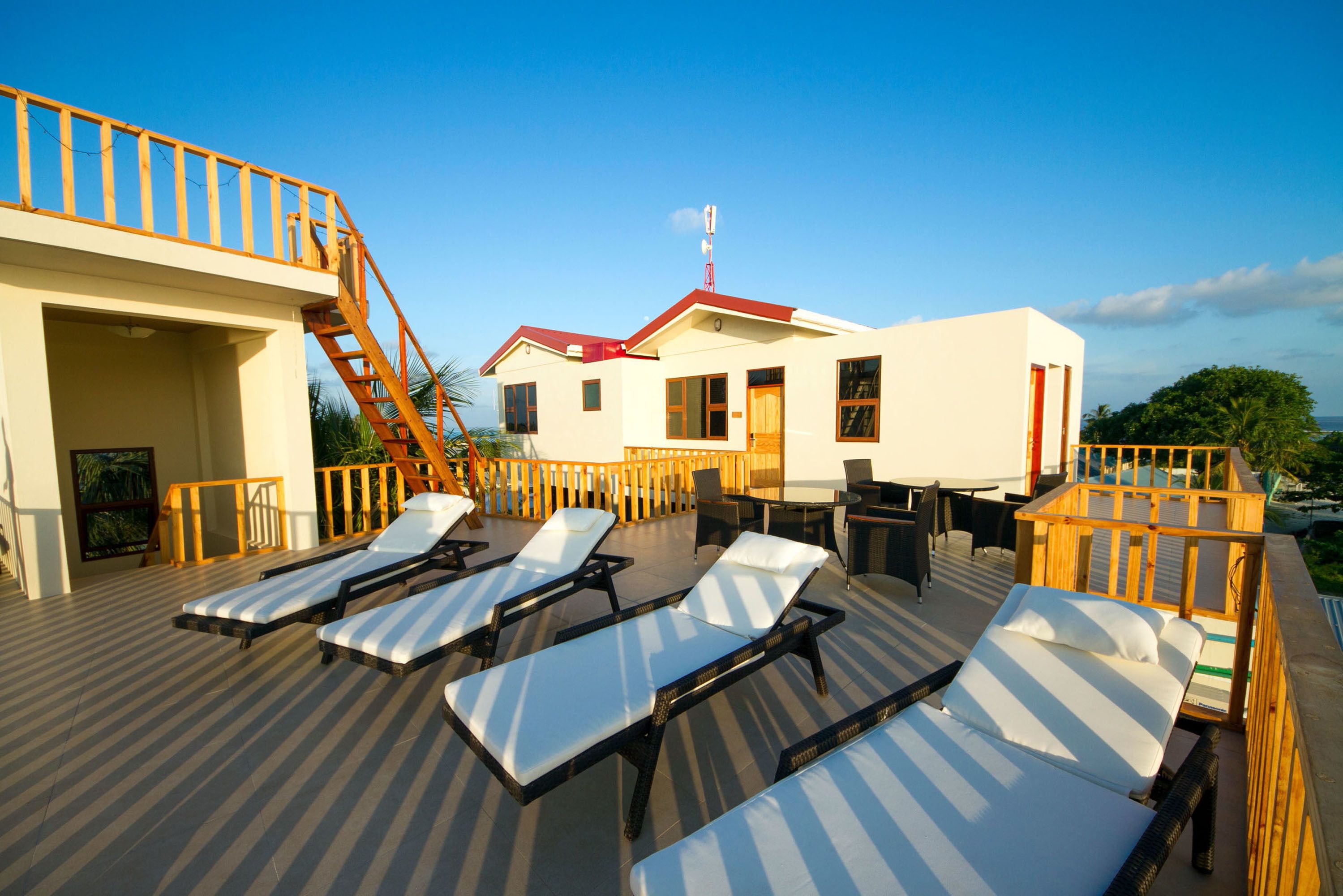 A rooftop deck with sun loungers, a wooden staircase, and a building with a red roof.