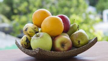 Un saladier rempli de fruits, notamment des pommes, des oranges et des poires, est posé sur une table en bois, avec un arrière-plan vert flou.