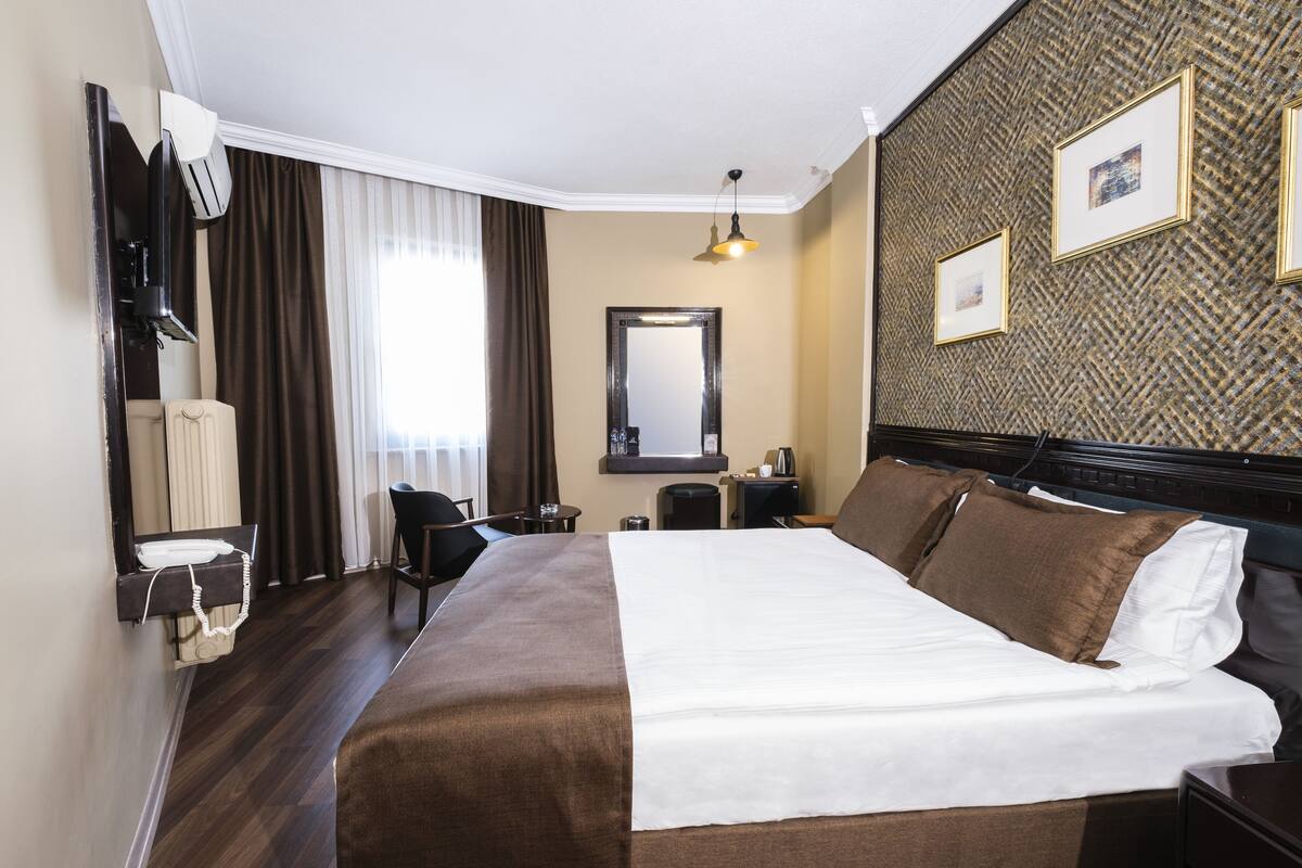A hotel room with a large bed, a desk, a chair, a TV, and a mirror.
