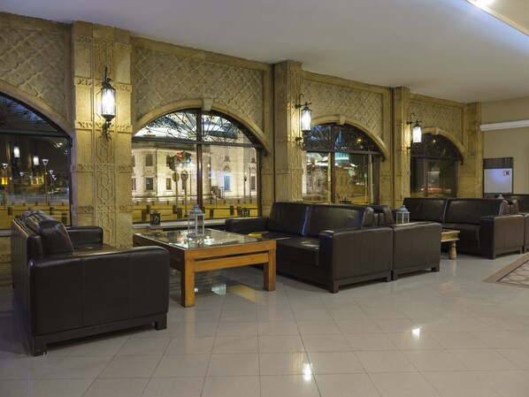 Un hall con asientos de cuero, una mesa de centro de vidrio y decoraciones ornamentales en las paredes.