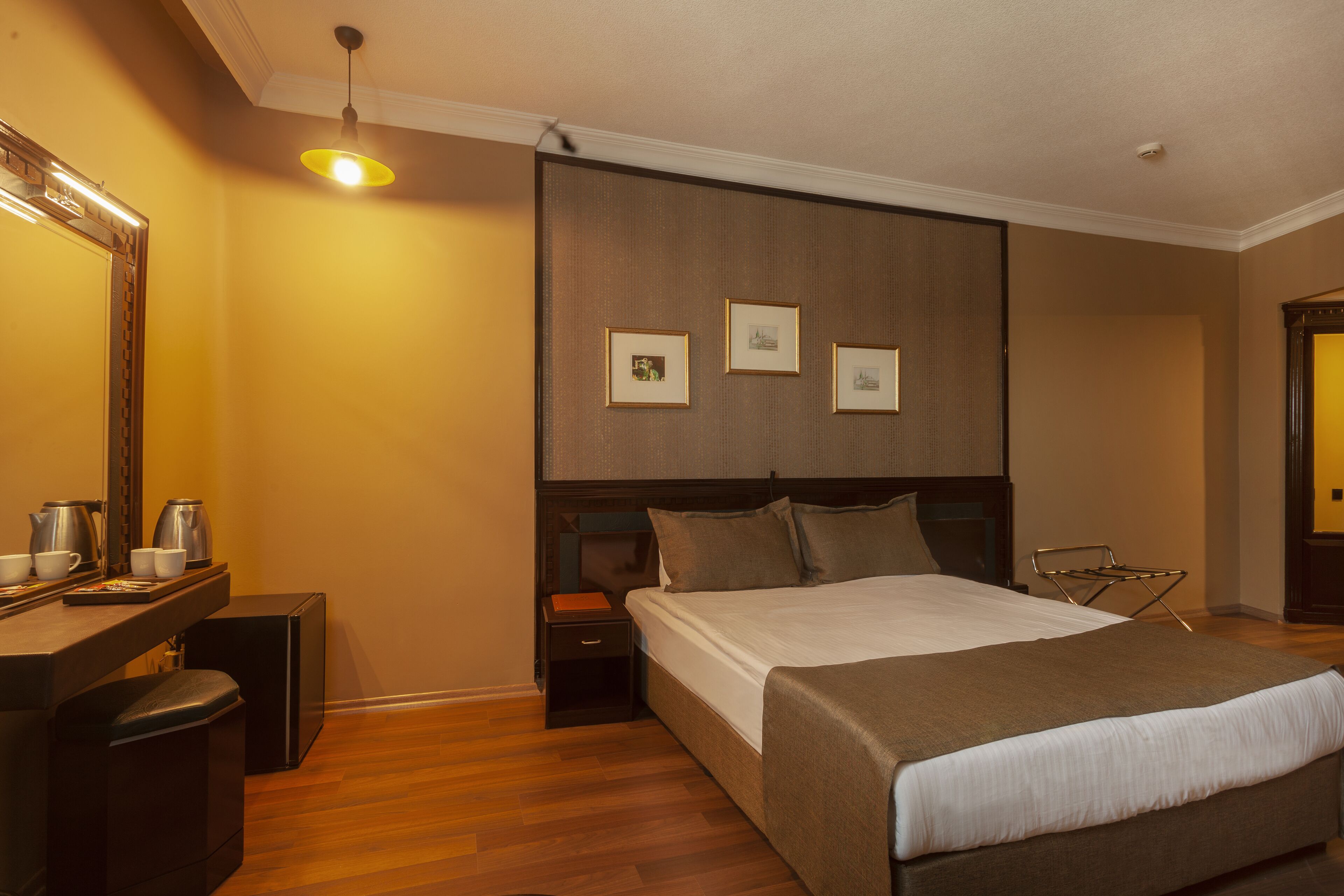Een hotelkamer met een groot bed, nachtkastjes, een bureau met spiegel en ingekaderde foto's aan de muur.