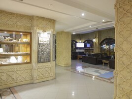 A spacious lobby with ornate wall carvings, a seating area with leather sofas, and a large display case with decorative items.
