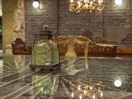 Una mesa con una lámpara de vidrio decorativa y una silla en una habitación con un candelabro y una pared de piedra.