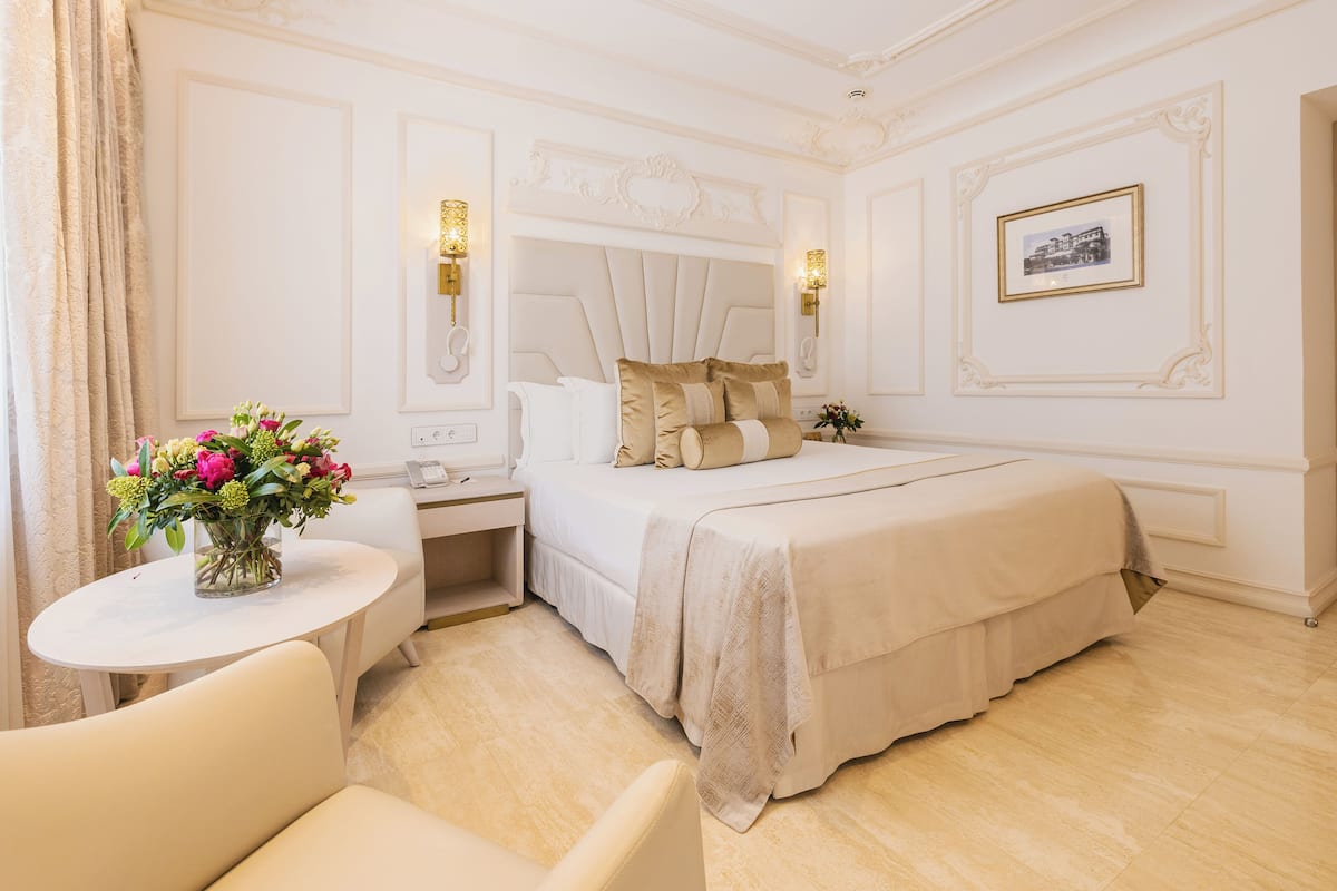 Habitación de hotel con una cama grande, una mesita de noche, una pequeña mesa redonda con un florero y una silla.