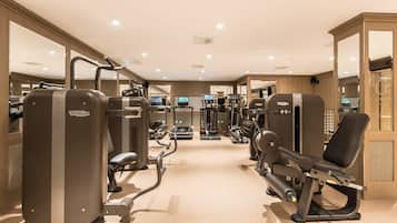 Un gimnasio con diversas máquinas de ejercicio, espejos y suelo de madera.