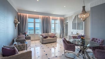 Ein modernes Wohnzimmer mit einer Couch, Sesseln, einem Glastisch und Meerblick durch große Fenster.