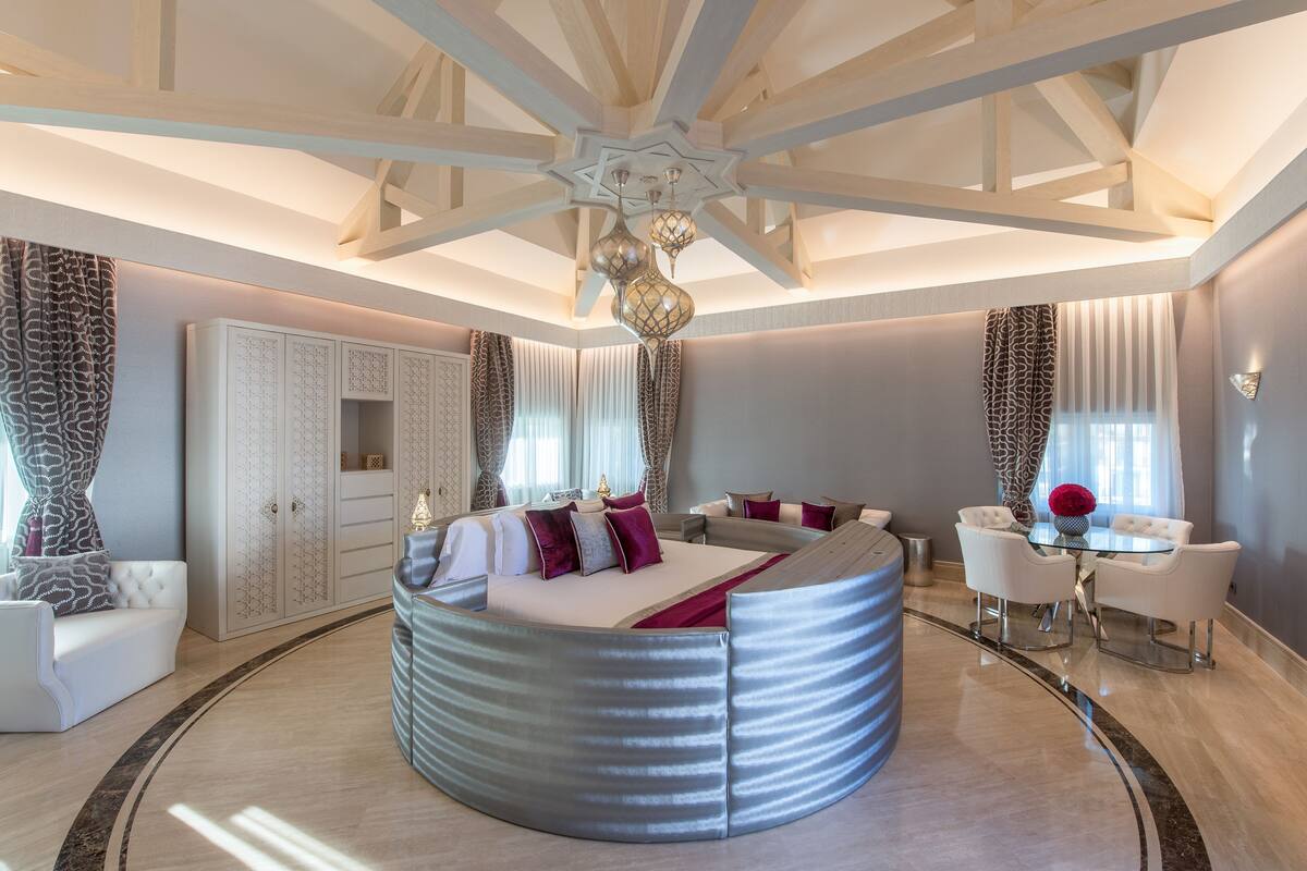 Un dormitorio moderno con una cama redonda, un armario grande y una zona de comedor con mesa y sillas.