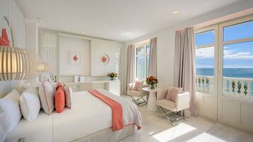 Habitación de hotel con una cama grande, un área de descanso con una mesa y sillas, y un balcón con vista al mar.