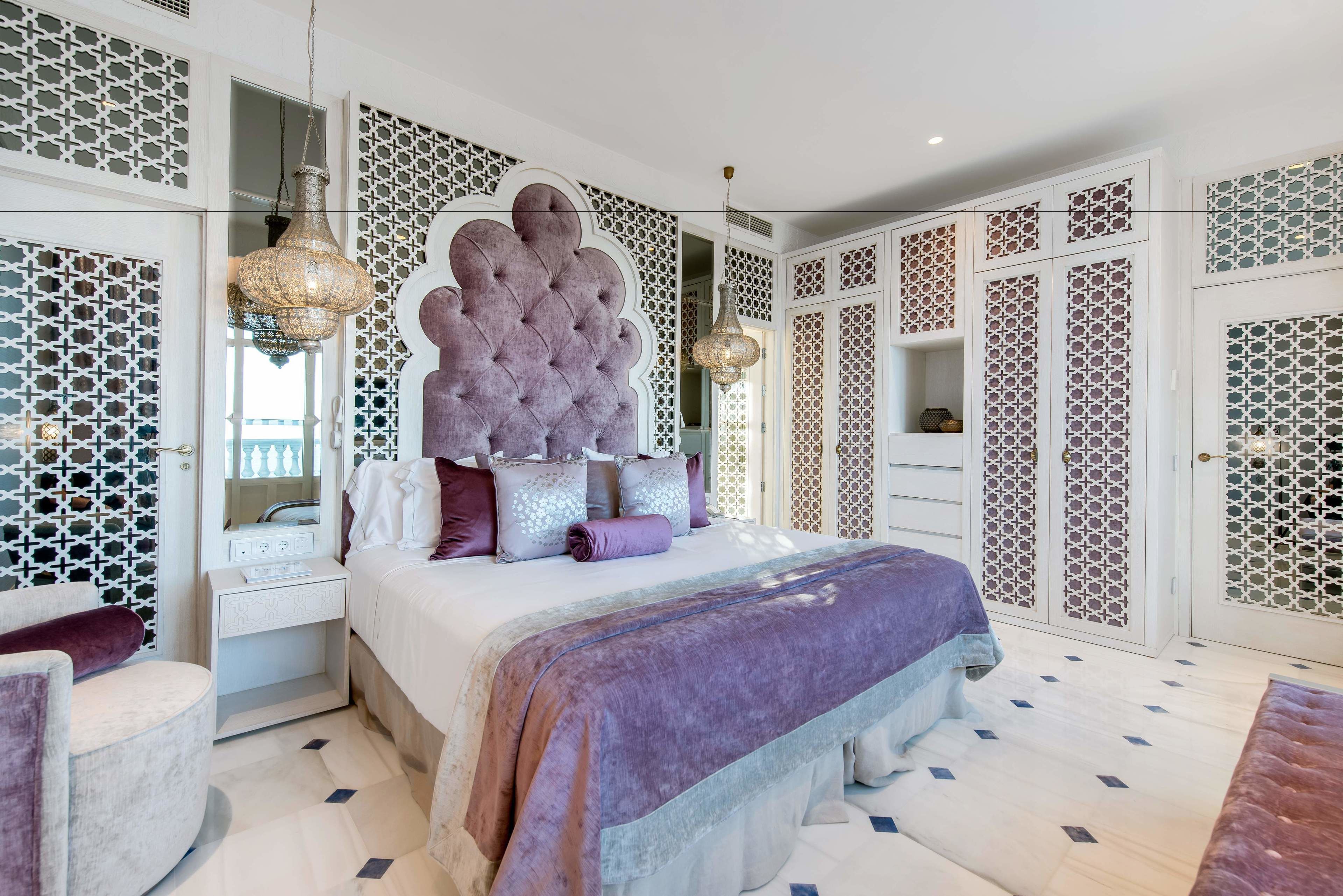 A bedroom with a large tufted headboard, a bed with multiple pillows, a bedside table, and a hanging lamp.