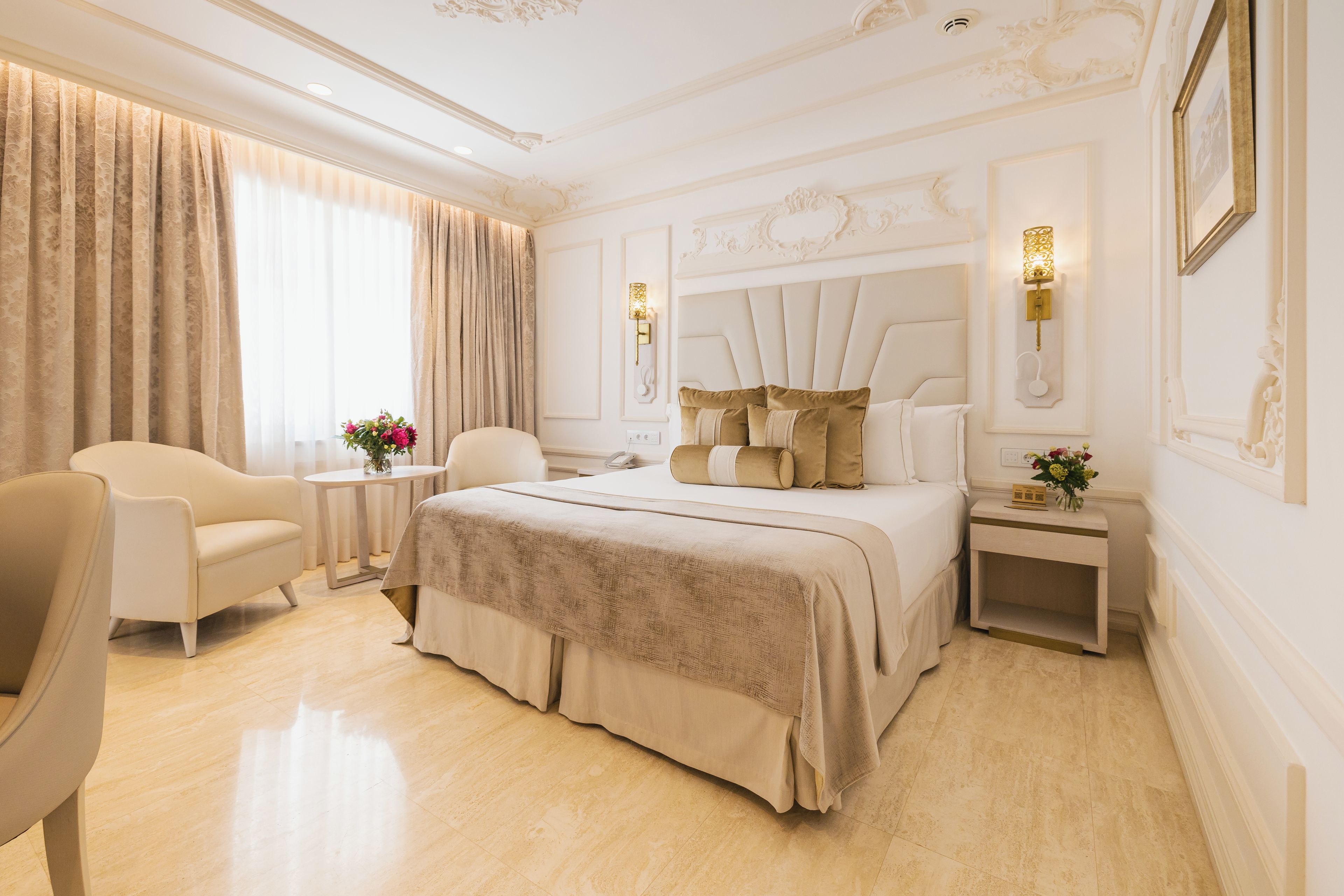Een hotelkamer met een groot bed, een zithoek met een stoel en een klein tafeltje, en een nachtkastje met een lamp.