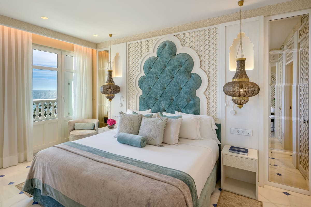 Un dormitorio amplio con una cama grande, vista al mar a través de una ventana y un panel decorativo en la pared.