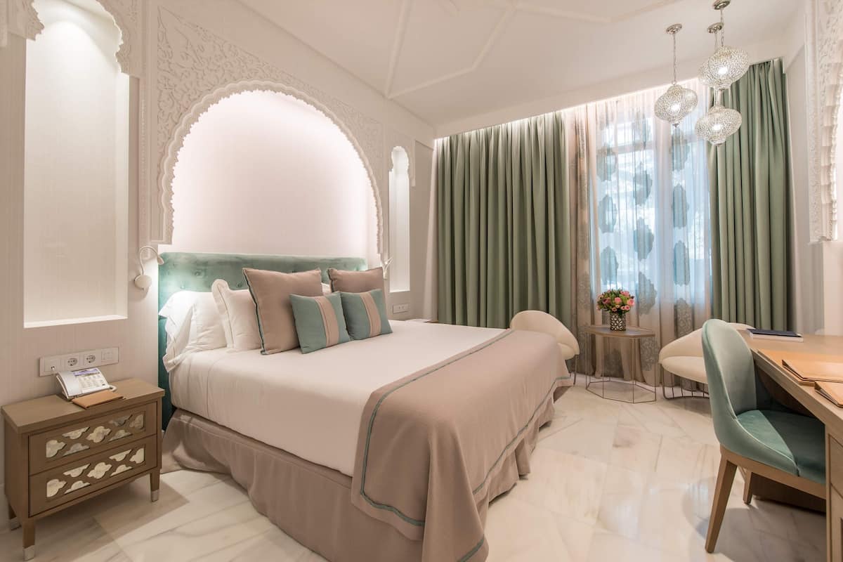 Un dormitorio con una cama grande, un escritorio y una silla. Hay una mesita con un jarrón de flores.