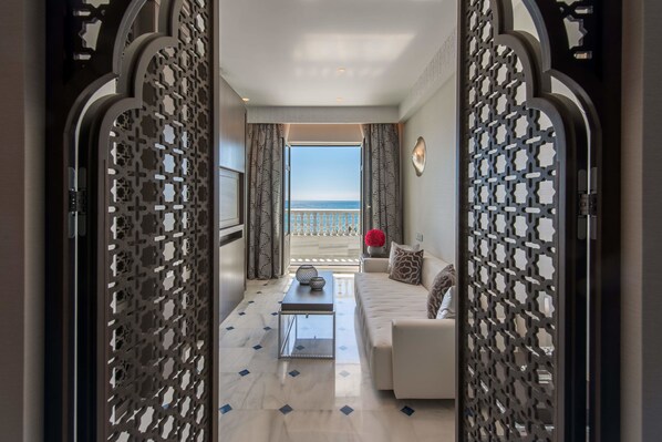 A modern hotel room with a balcony, a sofa, a coffee table, and decorative pillows. - Gran Hotel Miramar GL (Málaga)