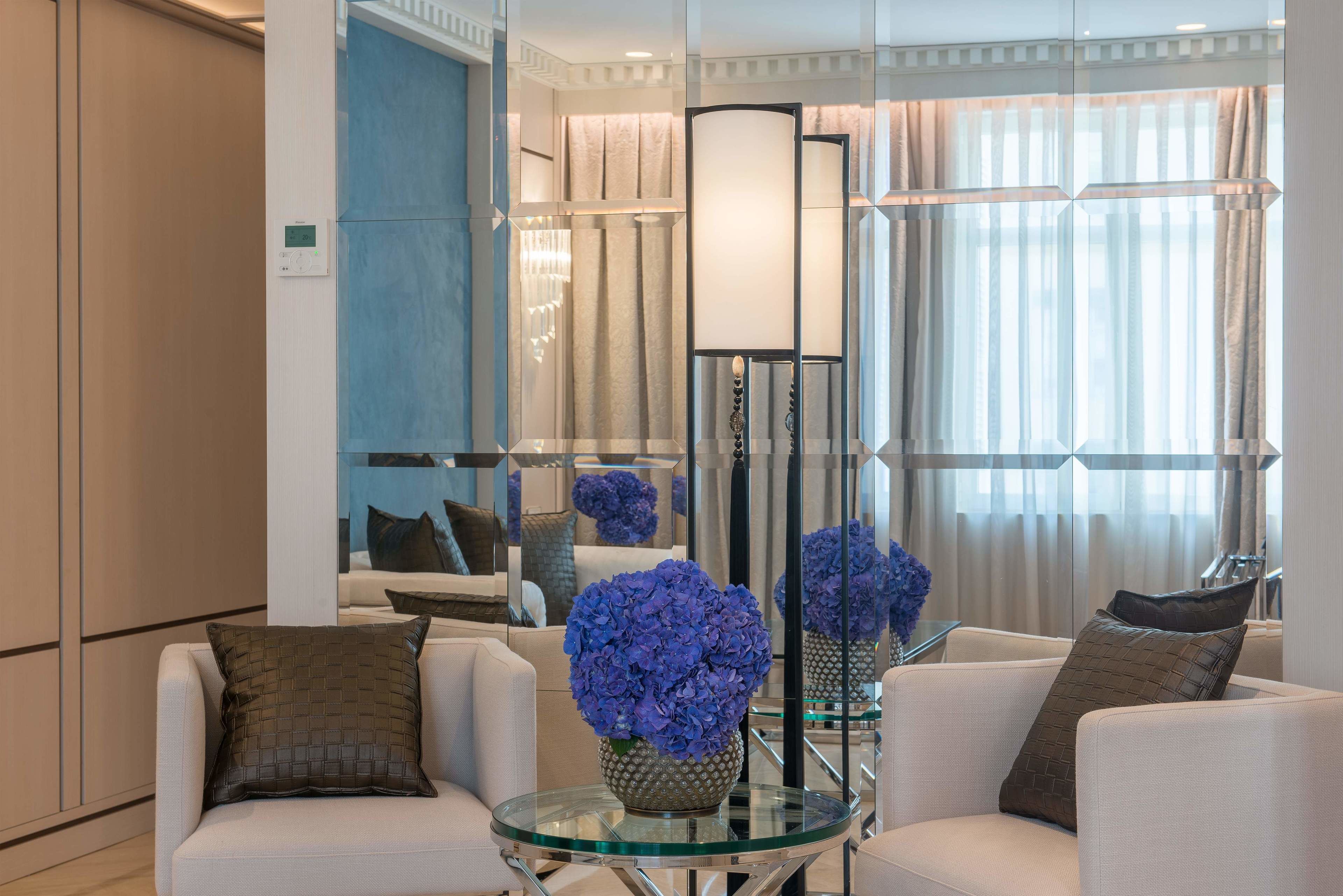 Una sala de estar moderna con una mesa de centro de vidrio, sofás blancos y un espejo grande que refleja la habitación.