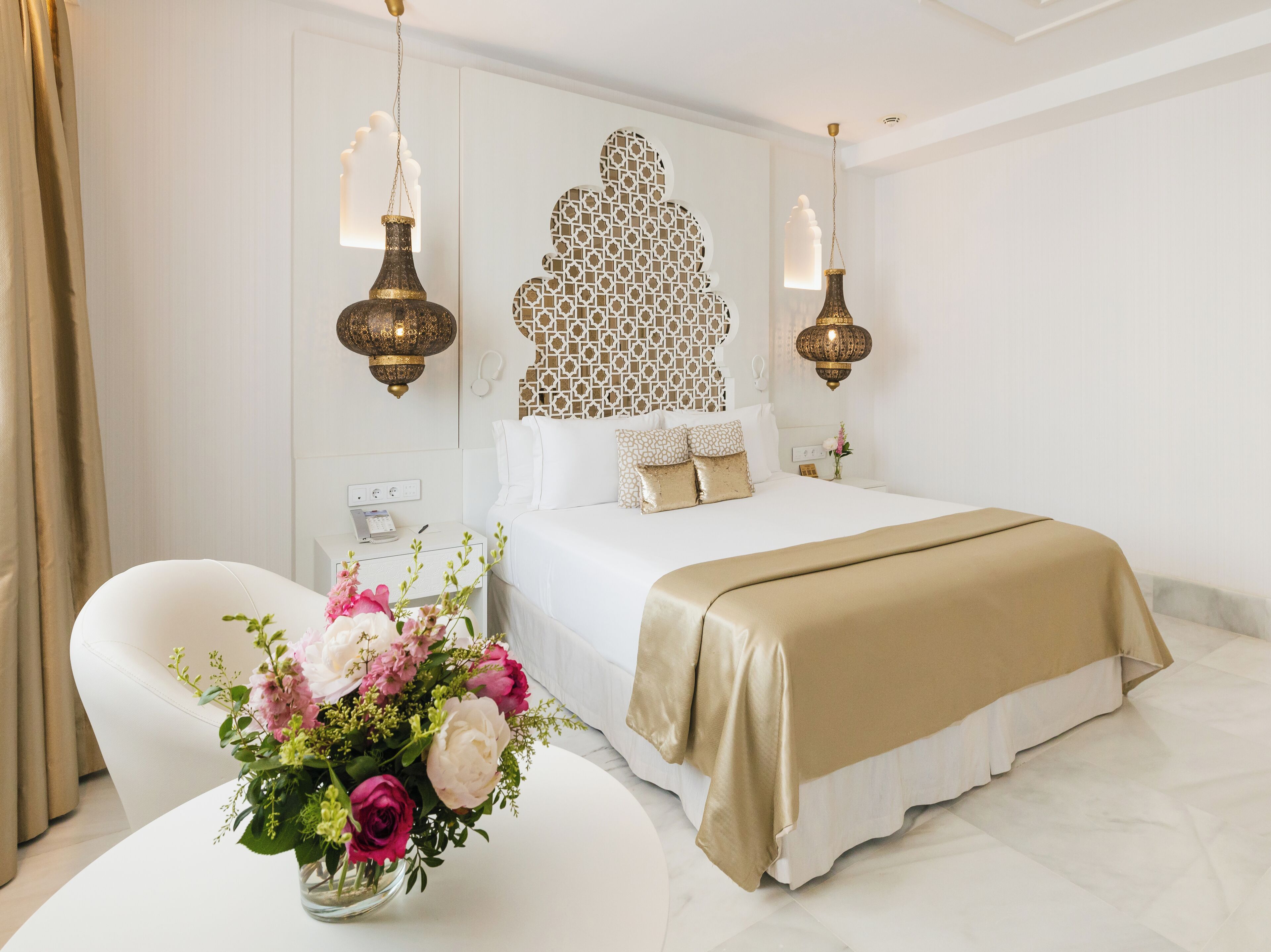 Ein Hotelzimmer mit einem großen Bett, einem Nachttisch mit Blumenvase und zwei Wandlampen.