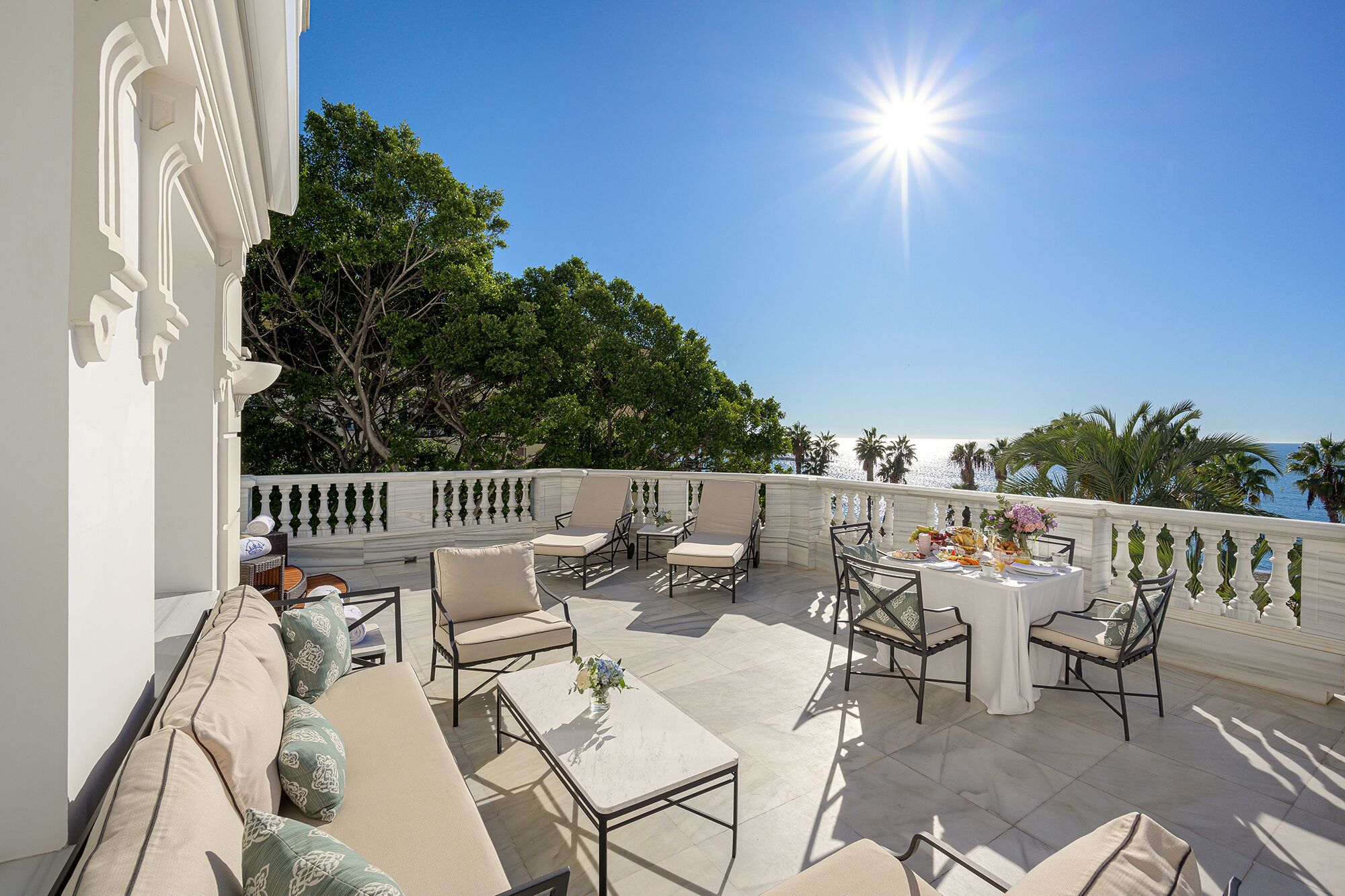 An outdoor patio with a dining table set for a meal, surrounded by chairs and sofas, overlooking a scenic view.