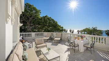 An outdoor patio with a dining table set for a meal, surrounded by chairs and sofas, overlooking a scenic view.