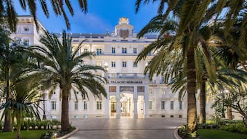 Un imposant bâtiment doté d’une entrée centrale, de palmiers et d’une enseigne indiquant « PALACIO MIRAMAR ».