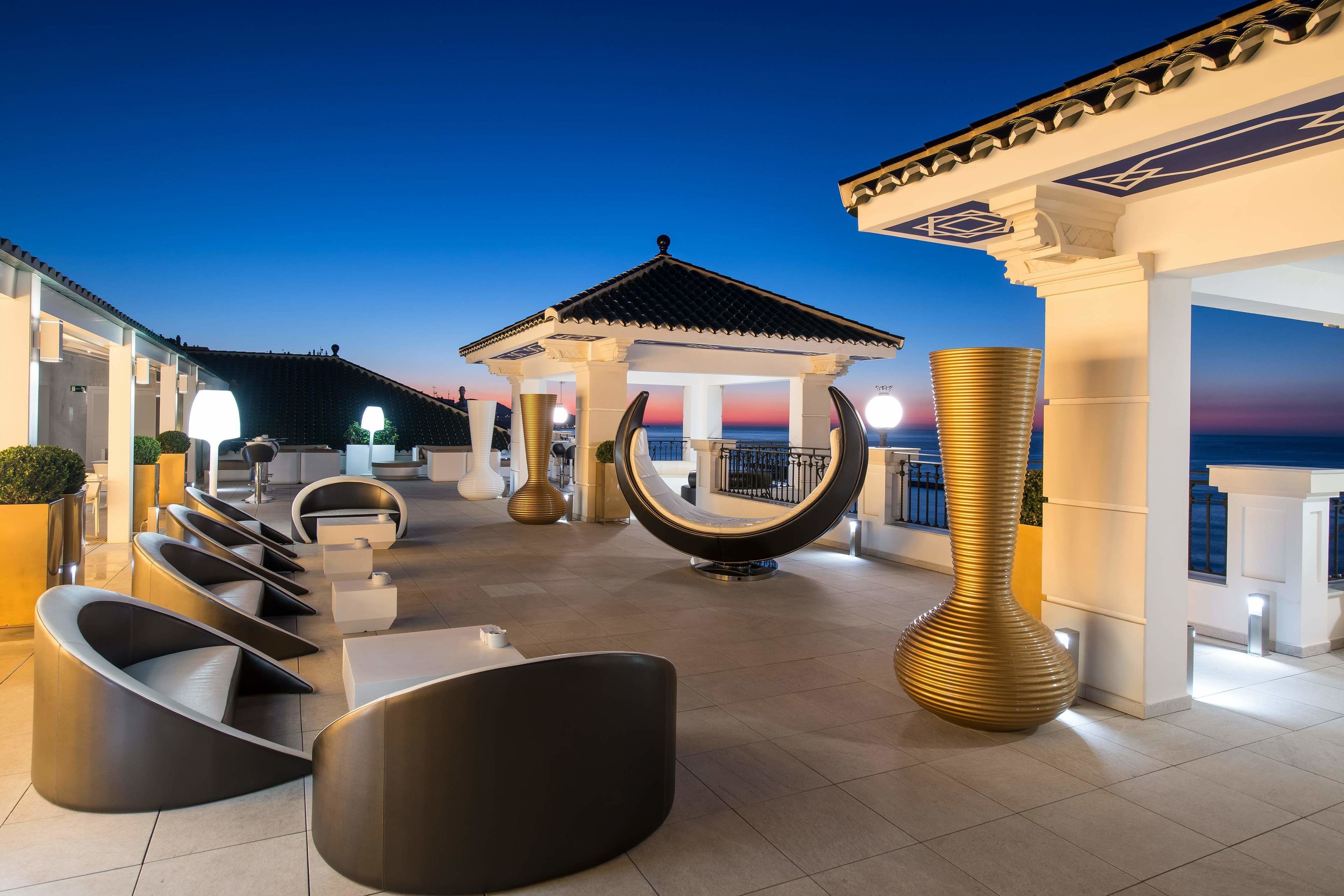 Una terraza en la azotea con mobiliario moderno, una fuente decorativa y vistas a la puesta de sol.