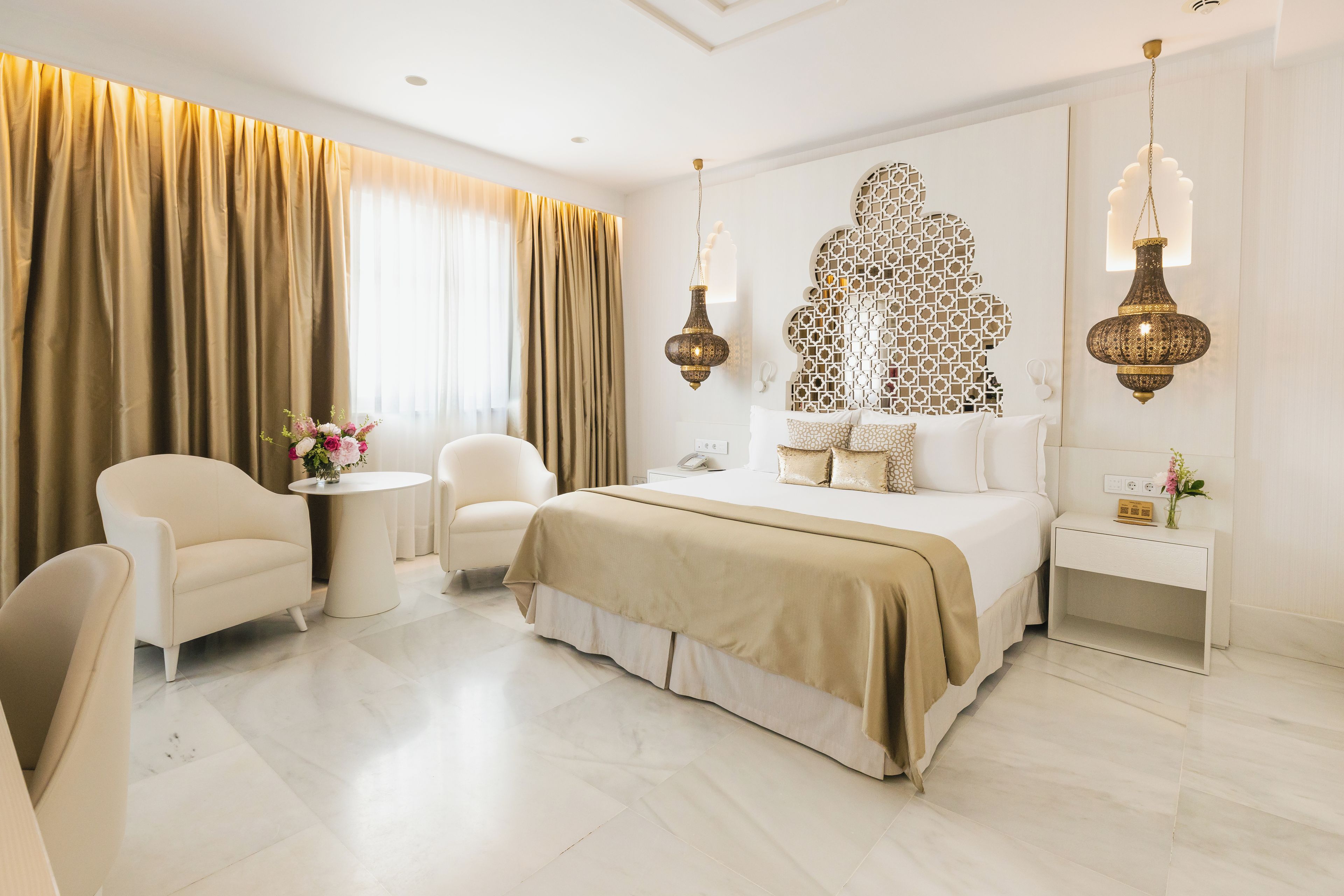 Habitación de hotel con una cama grande, dos sillones, una mesita con un florero y un panel decorativo en la pared.