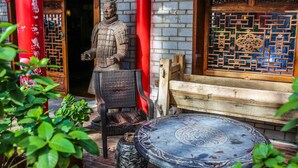 A traditional Chinese building with a statue, a wooden bench, and a table. - Xian Ancient City Youth Hostel (Xi'an)