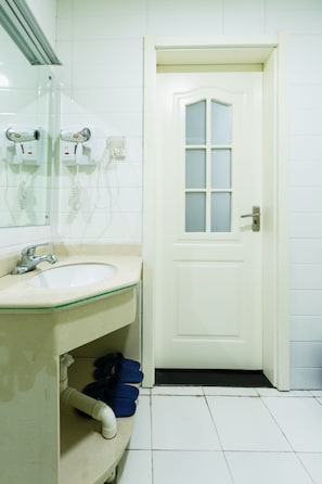 A bathroom with a white sink, a mirror, a door with a frosted glass window, and a pair of blue slippers on the floor. - Xian Ancient City Youth Hostel (Xi'an)