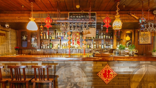A bar with wooden furniture, shelves with bottles, and hanging decorations. - Xian Ancient City Youth Hostel (Xi'an)