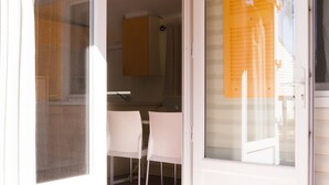 Puerta corredera de vidrio abierta que da a una cocina con armarios blancos y una silla blanca.