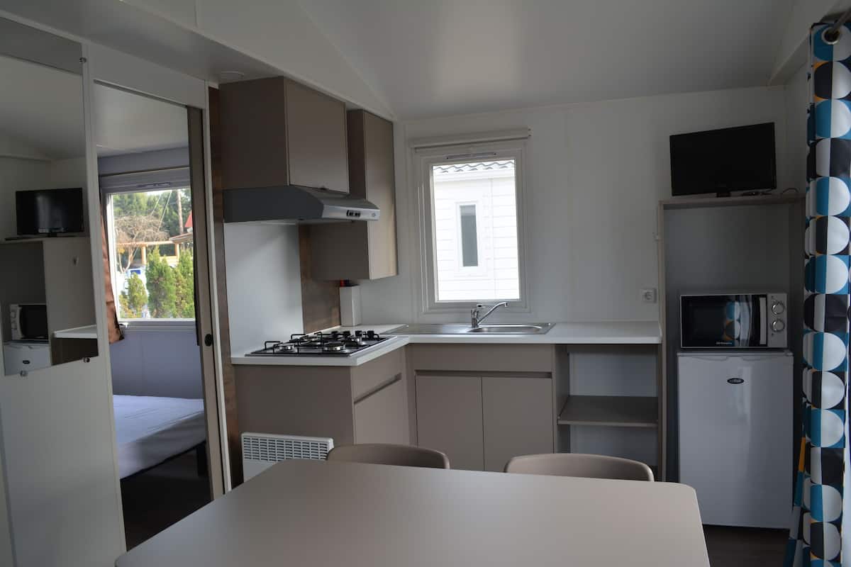 Eine kompakte Küche mit Herd, Spüle und Mikrowelle. Ein kleiner Kühlschrank und ein Fernseher sind über der Spüle angebracht.