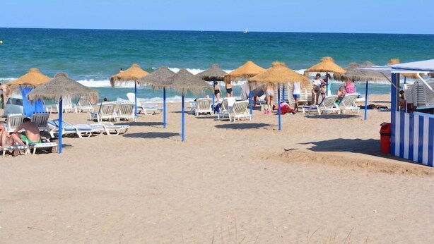 Una playa con tumbonas, sombrillas de paja y un pequeño quiosco.