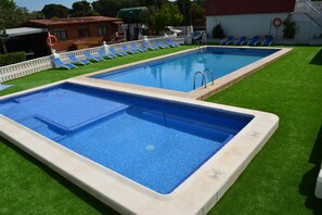 Two rectangular swimming pools with clear blue water, surrounded by green artificial grass and white poolside chairs. - Camping Valencia El Saler (Valencia)