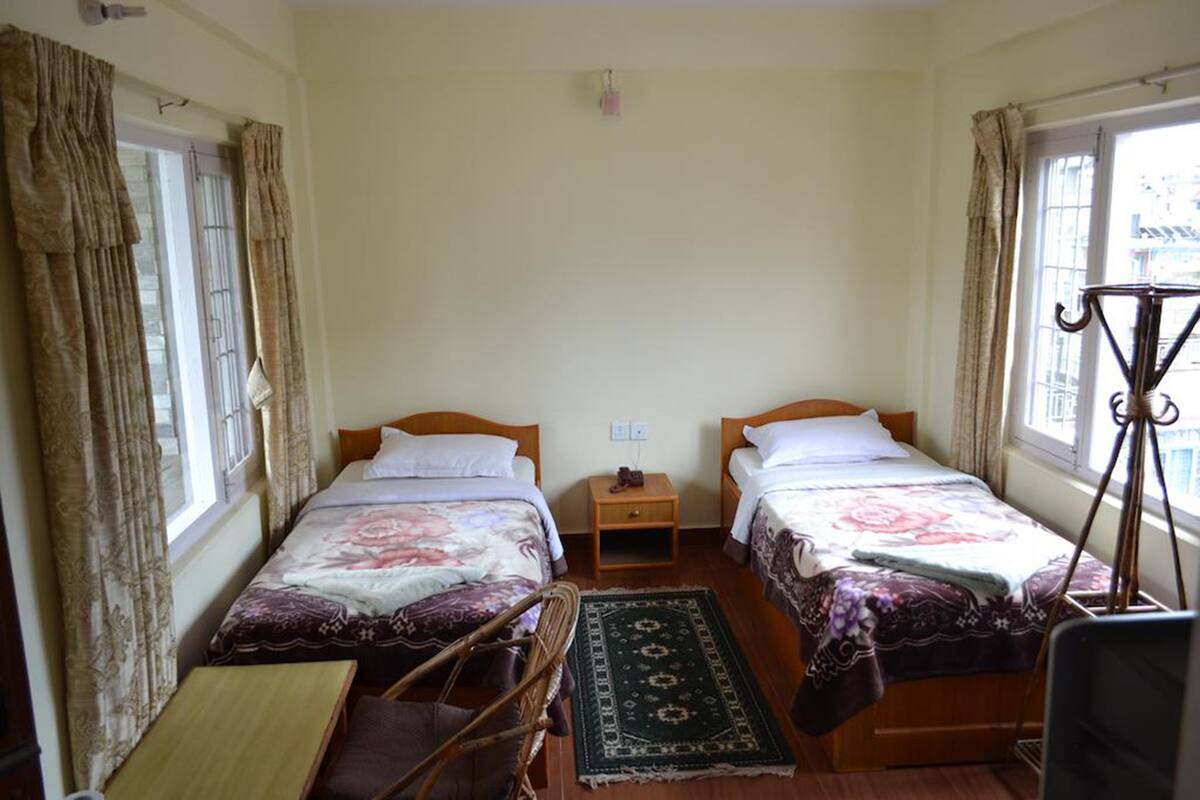A room with two beds, a small table, a chair, and a window with curtains.
