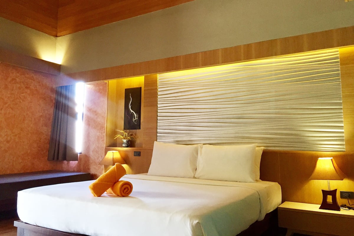 A hotel room with a large bed, two bedside lamps, a wall-mounted artwork, and a window with blinds.