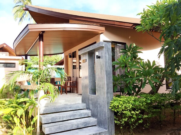 A modern building with a curved roof, a staircase leading to a covered entrance, and lush greenery surrounding the property.