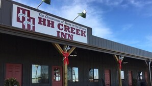 Rakennuksessa on HH Creek Inn -kyltti, ja sen julkisivu on pelkistetty, siinä on punaiset ovet ja ikkunat, ja sen yläpuolella on kirkas taivas.
