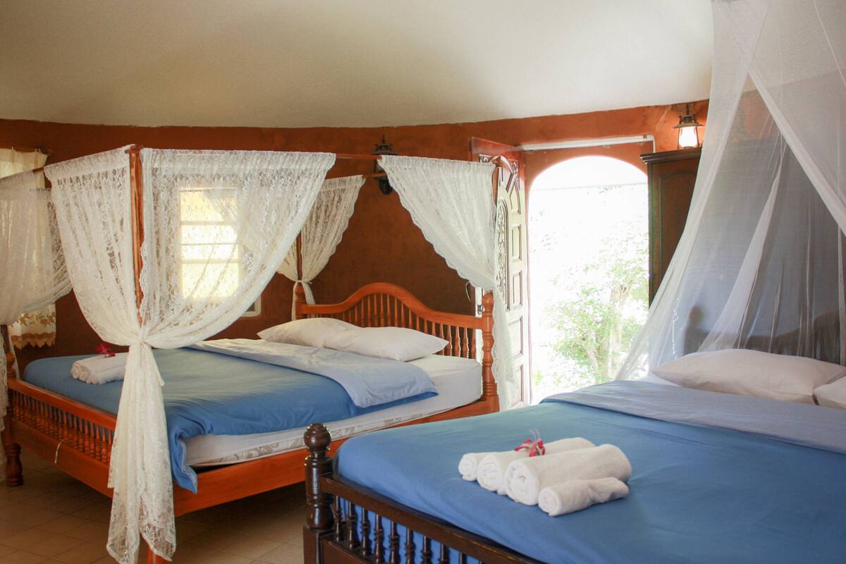 Ein Zimmer mit zwei hölzernen Betten, jeweils mit Baldachin und weißen Leinentüchern.
