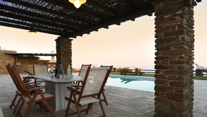 Een terras buiten met stenen zuilen, een zwembad en een bar met stoelen en flessen.