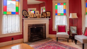 A living room with a fireplace, red walls, and a patterned rug. - River Run Bed and Breakfast (Fleischmanns)