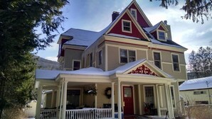 A two-story house with a red and beige exterior, a covered porch, and a snow-covered roof. - River Run Bed and Breakfast (Fleischmanns)