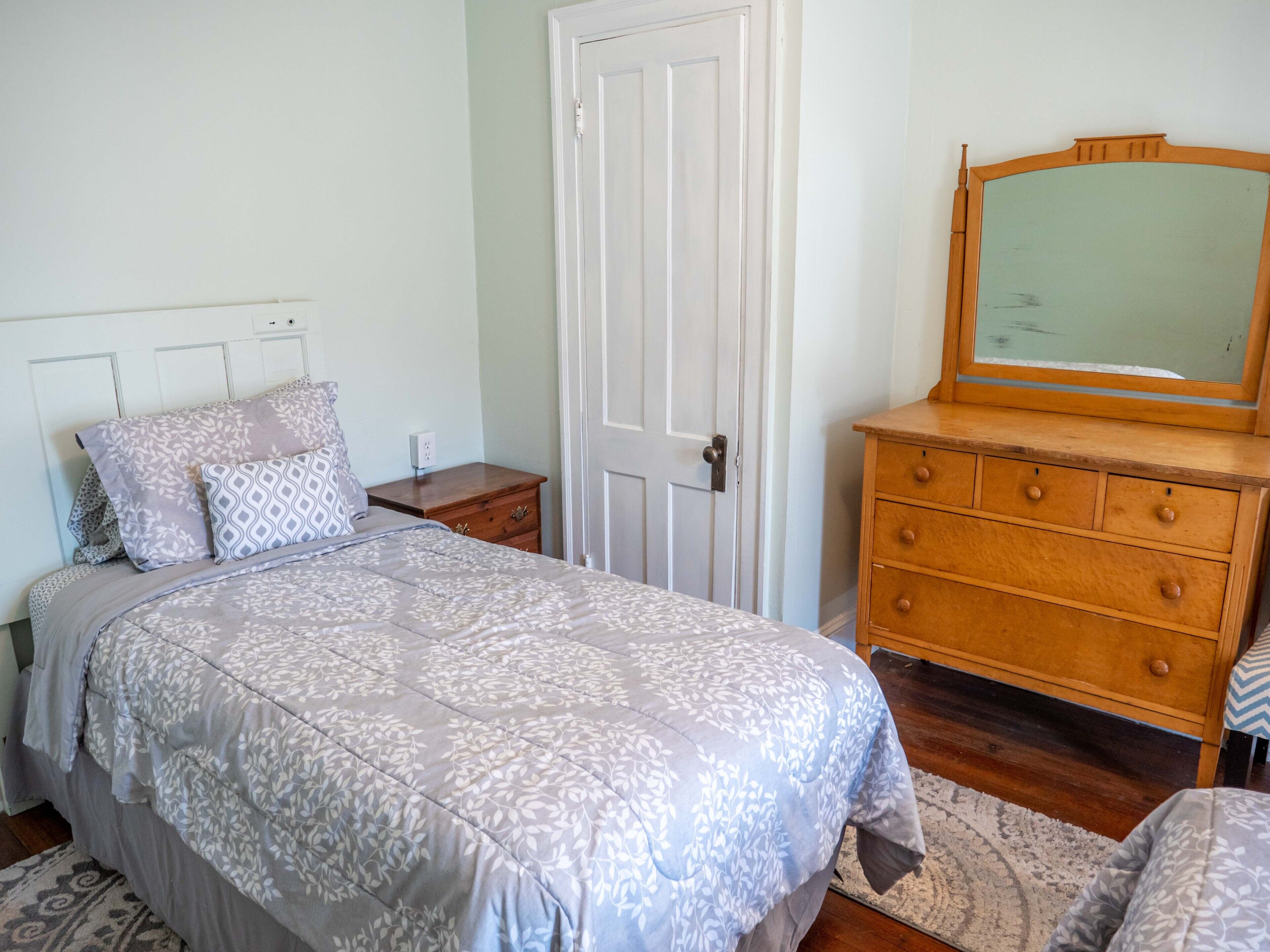 Une chambre à coucher avec un lit, une commode, un miroir et une porte.