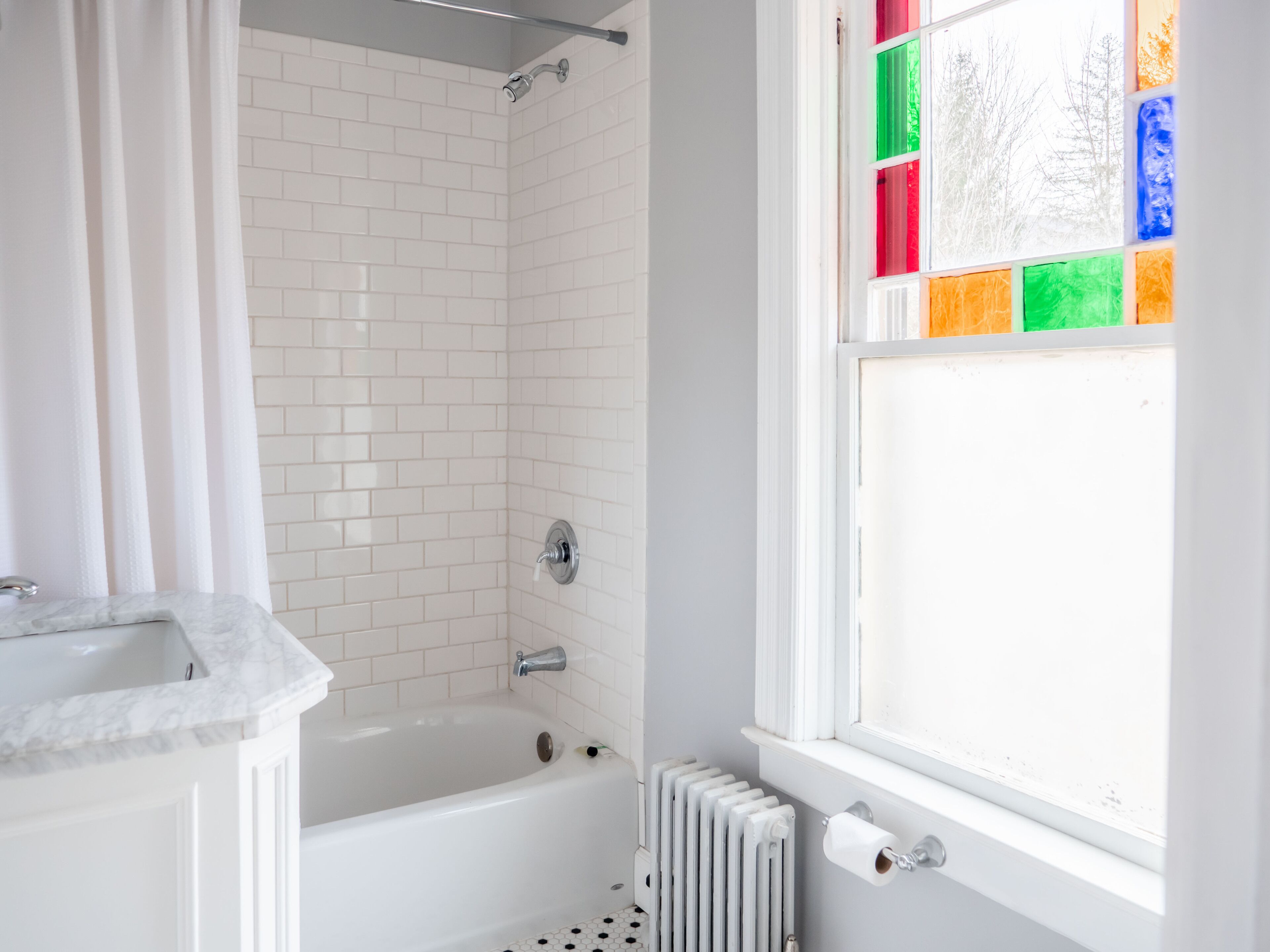 A bathroom with a white bathtub, a shower, a white sink, and a window with colorful stained glass.