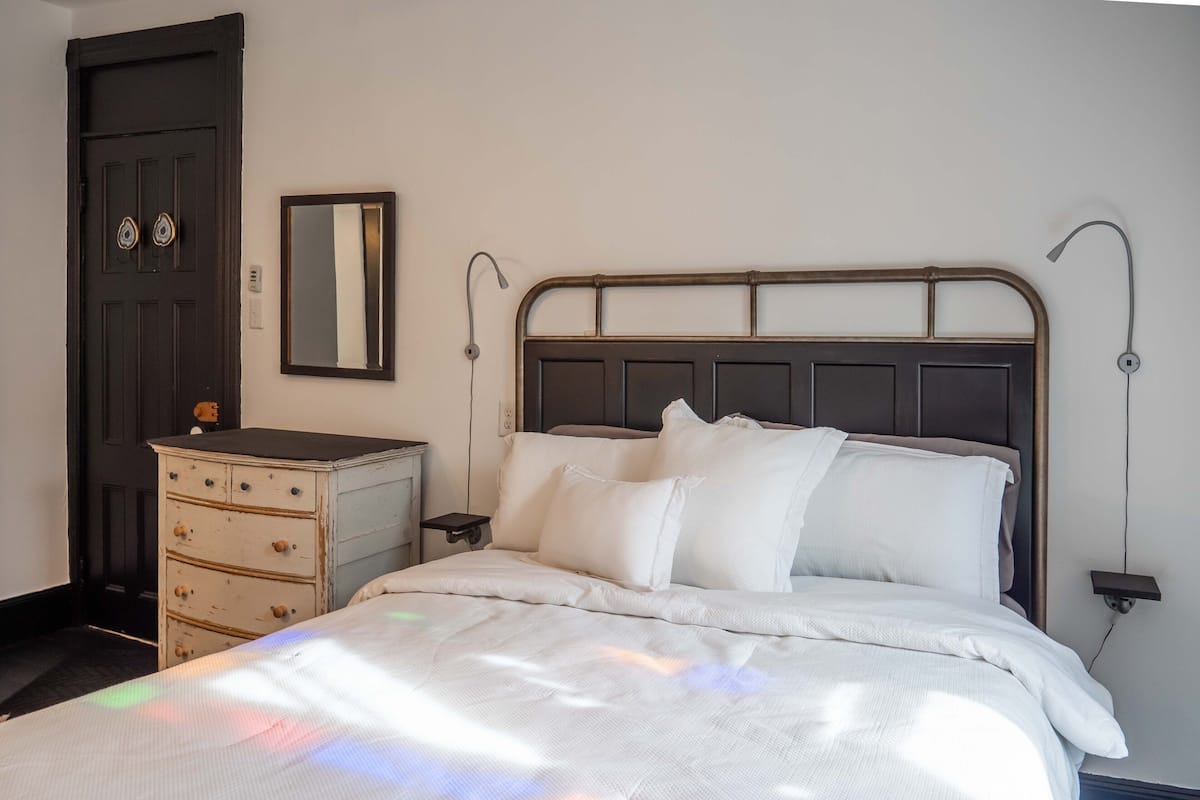 Un dormitorio con cama, mesitas de noche, cómoda, espejo y puerta.