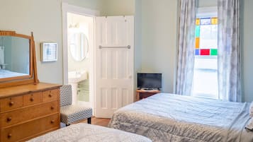 A bedroom with two beds, a dresser, a television, and a bathroom door.