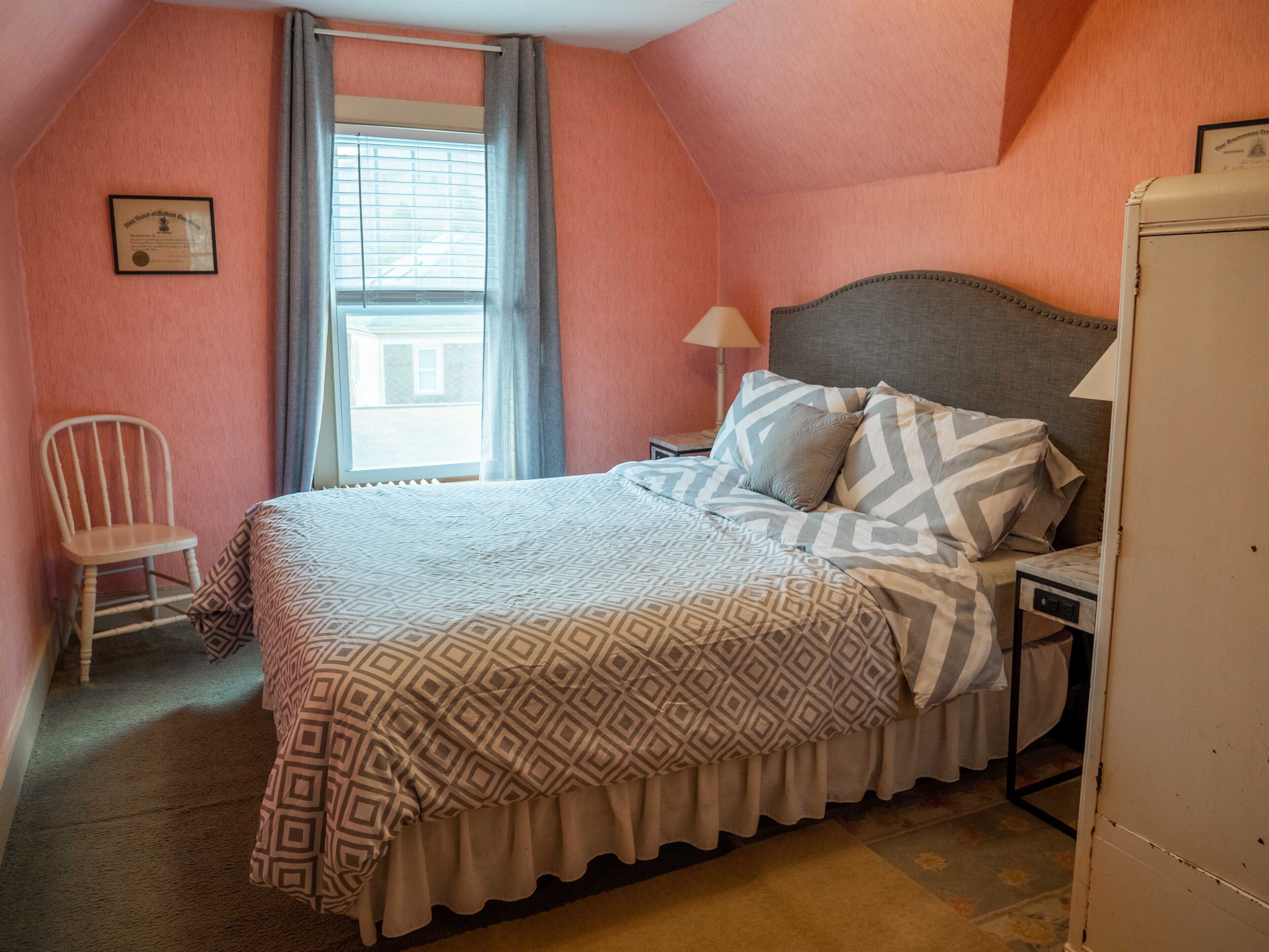 A bedroom with a bed, a chair, a nightstand, and a window.